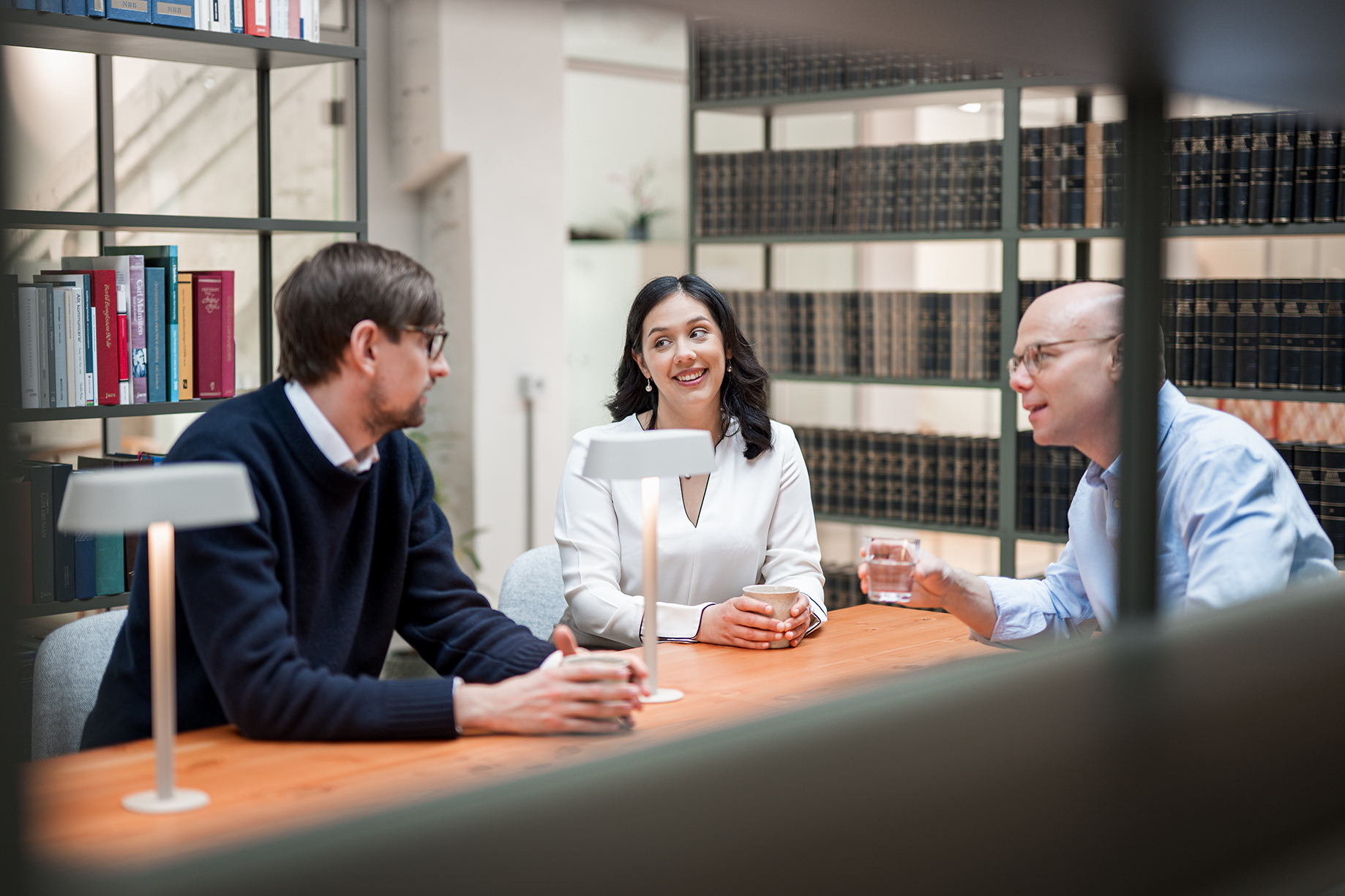 Tre personer sitter och pratar i ett bibliotek