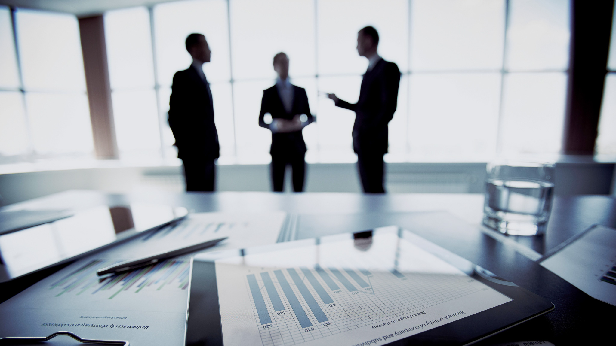 Skrivbord och tre affärsmän som diskuterar något